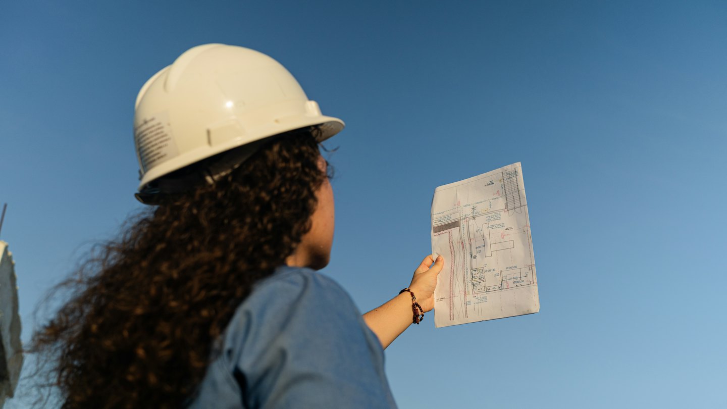 Engineer reviews architectural plans against blue sky.